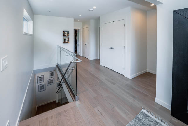 Bright hallway with wooden floors and glass railings leading to bedrooms. - Address WITHHELD, North Vancouver