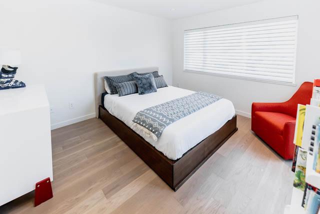 Bright bedroom with hardwood floors and a red chair, featuring a neatly made bed with blue and white bedding. - Address WITHHELD, North Vancouver