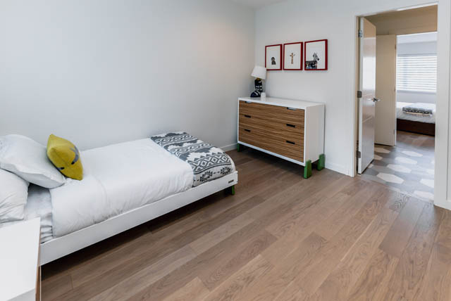 Bright bedroom with hardwood floors and a neatly made bed, featuring a dresser and framed artwork on the wall. - Address WITHHELD, North Vancouver
