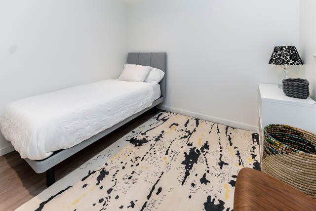 Bright bedroom with white bedding, patterned rug, and white nightstand. - Address WITHHELD, North Vancouver