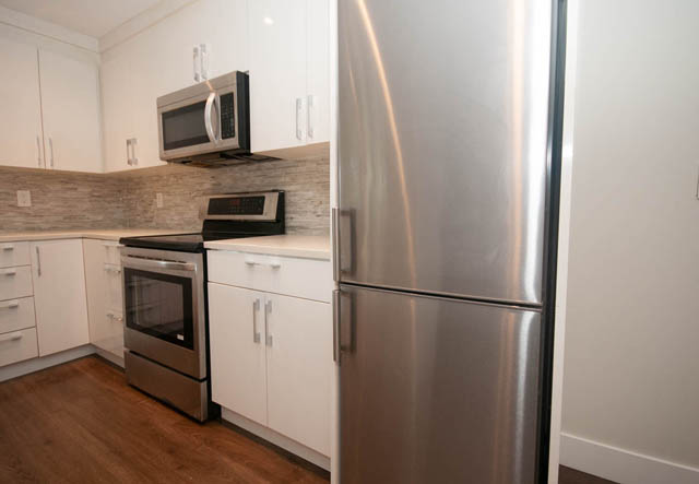 Bright kitchen with white cabinets, stainless steel appliances, and hardwood floors. - Suite - 4796 Skyline Dr, North Vancouver