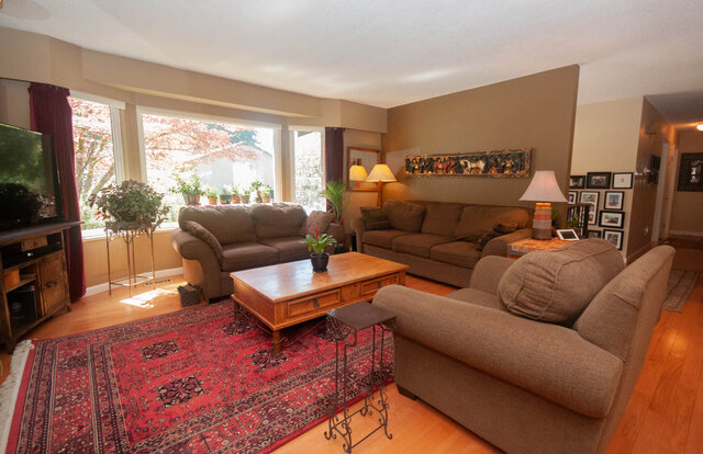 Spacious living room with hardwood floors, large windows, and a cozy sofa set. - Upper - 2352 Riverbank Pl, North Vancouver