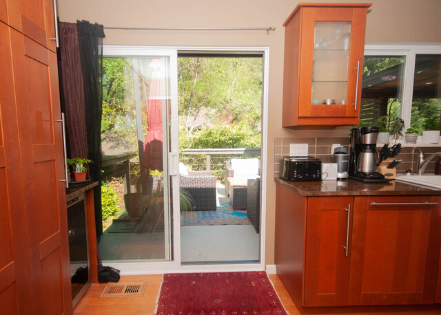 Bright kitchen with wooden cabinets, granite countertops, and a sliding glass door leading to a patio. - Upper - 2352 Riverbank Pl, North Vancouver