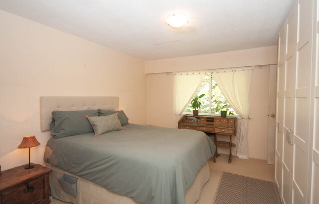 Spacious bedroom with light green bedding and wooden furniture, featuring a large window with sheer curtains.