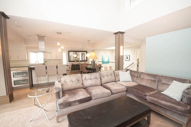 Spacious living room with plush sofas and modern decor, featuring hardwood floors and a kitchen in the background.