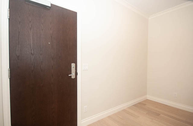 Bright hallway leading to a 2-bedroom condo with hardwood floors and a dark wooden door. - 404 - 185 Victory Ship Way, North Vancouver