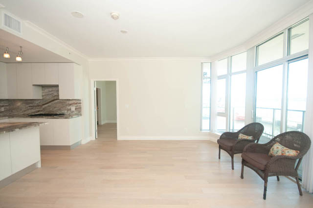 Bright living room with hardwood floors and large windows offering a city view. - 404 - 185 Victory Ship Way, North Vancouver