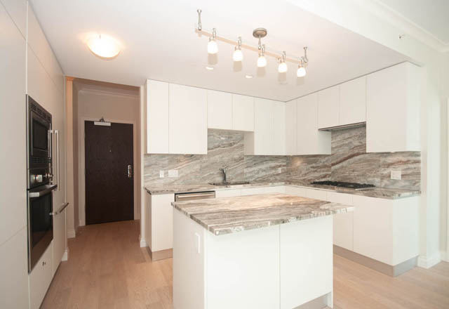 Bright kitchen with marble countertops and white cabinetry, hardwood floors. - 404 - 185 Victory Ship Way, North Vancouver