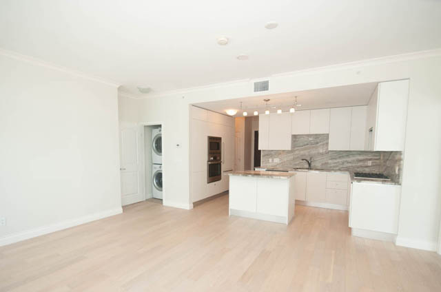 Bright kitchen with white cabinets, granite countertops, and hardwood floors. - 404 - 185 Victory Ship Way, North Vancouver