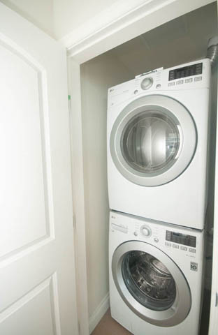 Compact laundry room with stacked washer and dryer, white walls, and a door leading in. - 404 - 185 Victory Ship Way, North Vancouver