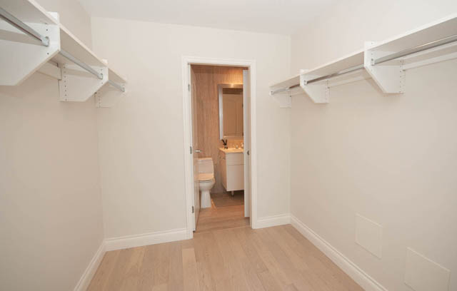 Bright walk-in closet with white walls, hardwood floors, and built-in shelves. - 404 - 185 Victory Ship Way, North Vancouver