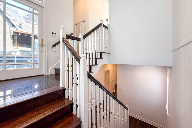 Staircase with white balusters and dark wood handrails, hardwood floors, and city view through glass door. - 2307 Marine Drive, West Vancouver