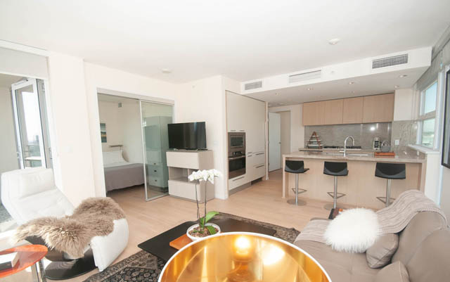 Bright kitchen with light wood cabinets and modern appliances, open to a cozy living area with plush seating and hardwood...