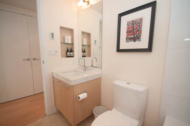 Furnished bathroom with wooden cabinets, marble countertops, and a framed artwork above the toilet.