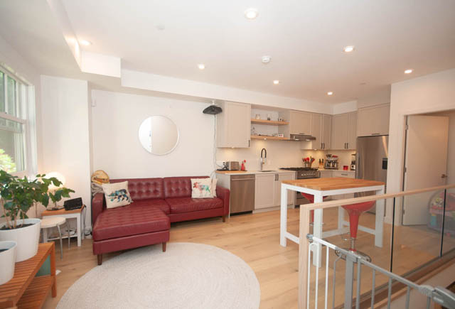 Open-concept living area with hardwood floors, modern kitchen, and red furniture. - 114 West 14th Ave, Vancouver West Side