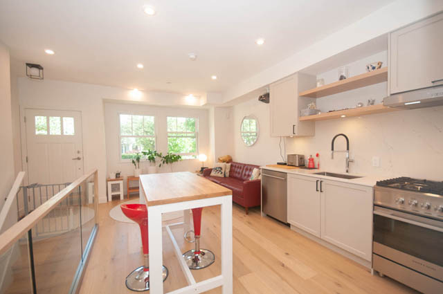 Bright kitchen with white cabinets, hardwood floors, and a red accent chair. - 114 West 14th Ave, Vancouver West Side