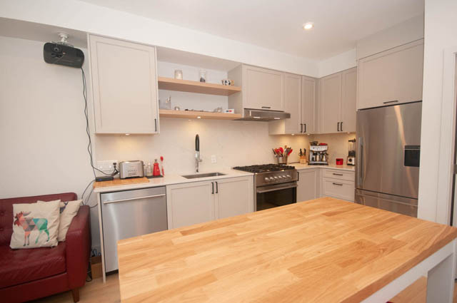 Bright kitchen with light wood countertops and white cabinets, modern appliances, and a cozy red bench. - 114 West 14th Ave, Vancouver West Side