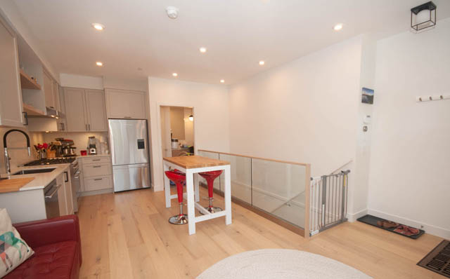 Bright kitchen with stainless steel appliances and hardwood floors, open to a cozy living area with a red couch.