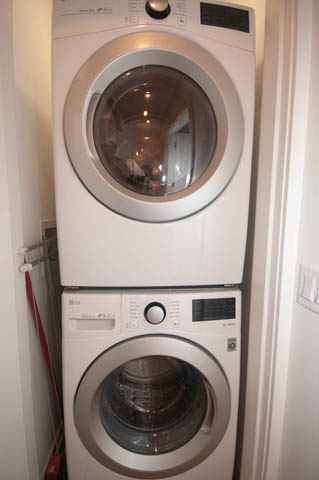 Bright laundry room with stacked washer and dryer, white walls, and a red hose visible. - 114 West 14th Ave, Vancouver West Side
