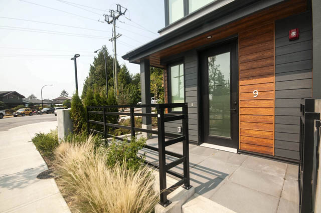 Modern townhouse entry with sleek black door, wood paneling, and stylish black railing. - 9 - 528 East 2nd, North Vancouver