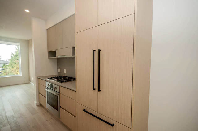 Modern kitchen with light wood cabinets, black handles, and a gas stove, featuring hardwood floors and a city view.