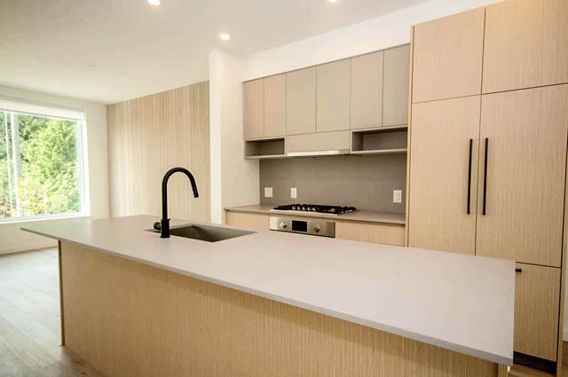 Modern kitchen with light wood cabinets, white countertops, and a large island, featuring a sleek sink and a city view.