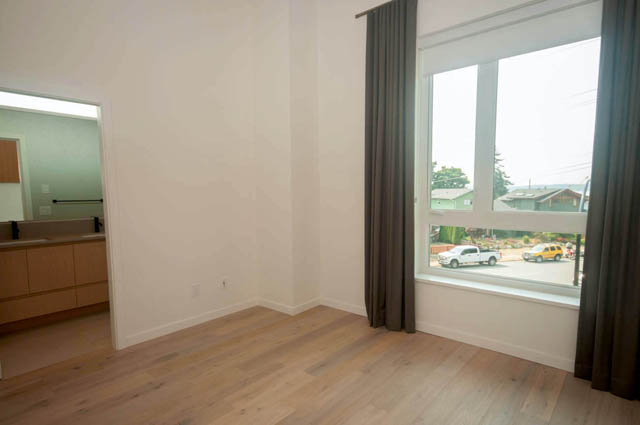 Spacious living room with hardwood floors, large window offering a city view, and a glimpse of a modern kitchen. - 9 - 528 East 2nd, North Vancouver