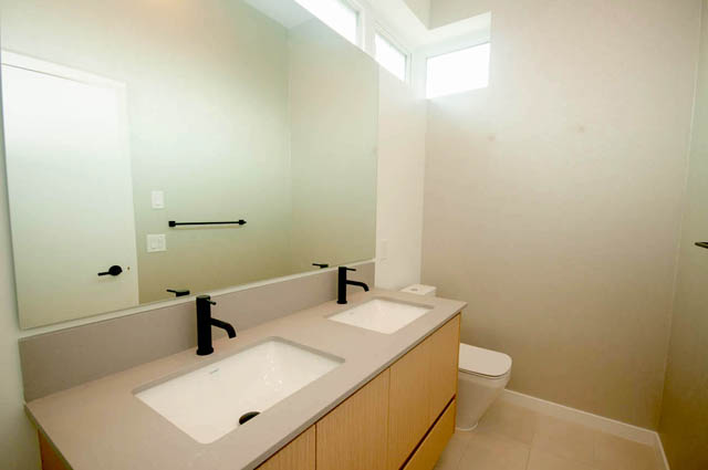 Modern bathroom with dual sinks, light wood cabinets, and a large mirror. - 9 - 528 East 2nd, North Vancouver