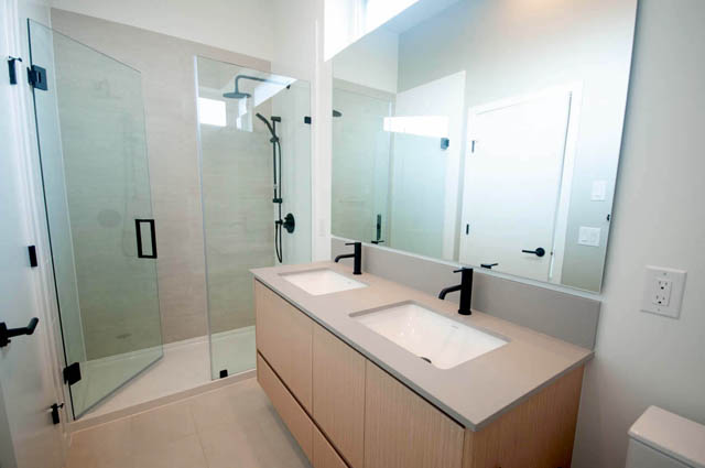 Modern bathroom with dual sink vanity, glass shower, and large mirror. - 9 - 528 East 2nd, North Vancouver