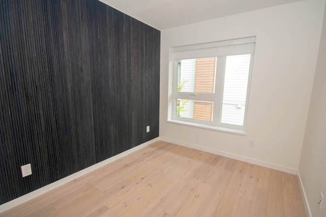 Spacious bedroom with dark accent wall and large window, featuring hardwood floors and a cozy ambiance. - 9 - 528 East 2nd, North Vancouver
