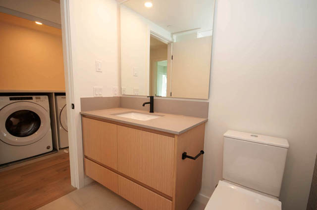 Modern bathroom with light wood vanity, white countertop, and large mirror. - 9 - 528 East 2nd, North Vancouver