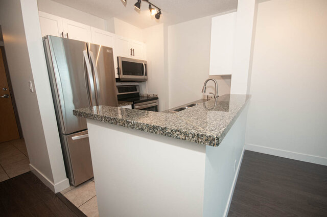 Modern kitchen with granite countertops and stainless steel appliances, featuring a sleek island and hardwood floors.