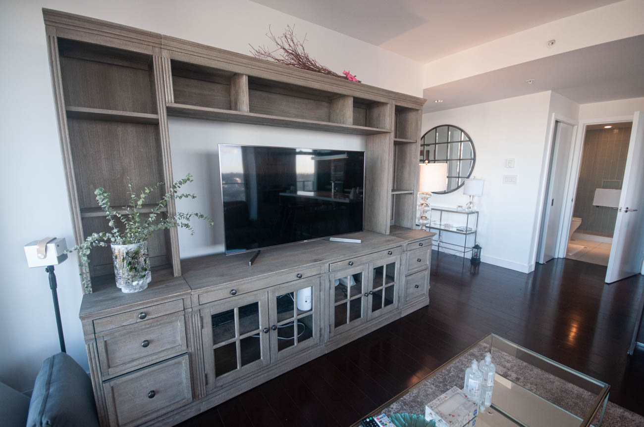 Furnished living room with a large TV mounted in a wooden entertainment center, hardwood floors, and a city view.