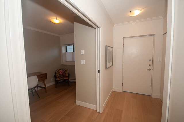 Spacious hallway leading to a cozy bedroom with hardwood floors and a floral armchair. - 308 - 1688 Cypress Street, Vancouver West Side