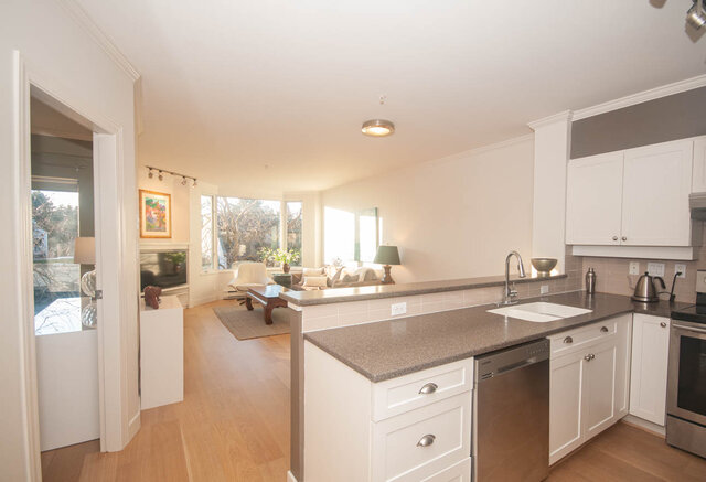 Bright kitchen with white cabinetry, granite countertops, hardwood floors, and a view of the living area.