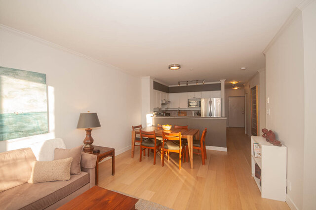 Open-concept living space with hardwood floors, a cozy sofa, and a modern kitchen with white cabinets and stainless steel...