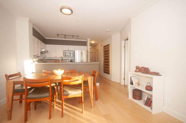 Bright kitchen with light wood dining table and chairs, hardwood floors, and a cozy living area with a Buddha statue.