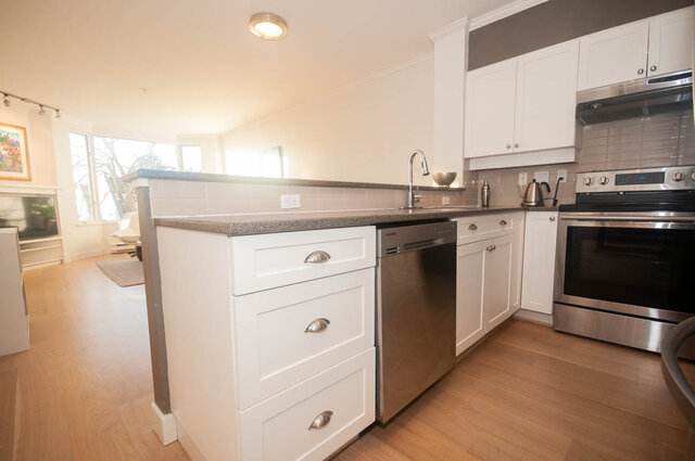 Bright kitchen with white cabinetry, granite countertops, stainless steel appliances, and hardwood floors.