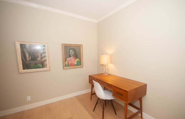 Spacious bedroom with wooden desk, chair, and framed portraits on the wall, featuring hardwood floors.