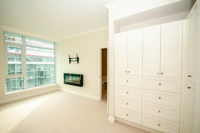 Spacious bedroom with built-in white cabinetry and a large window offering a city view. - 912 - 175 Victory Ship Way, North Vancouver