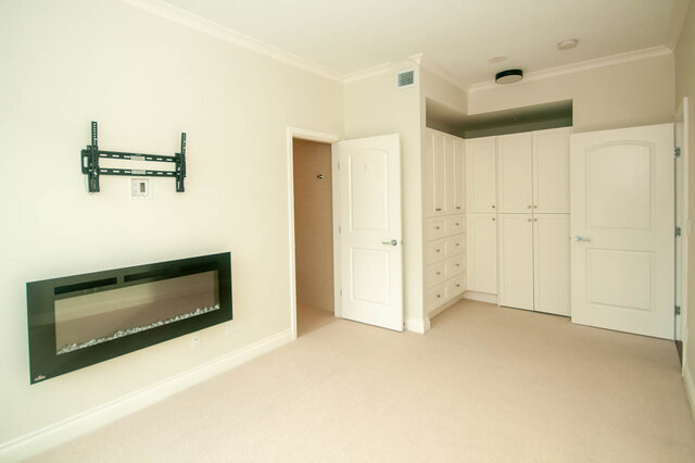 Spacious bedroom with a fireplace, wall-mounted TV, and ample closet space. - 912 - 175 Victory Ship Way, North Vancouver