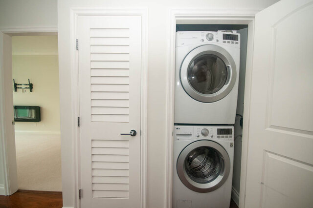 Efficient laundry room with stacked washer and dryer, white louvered doors, and hardwood floors. - 912 - 175 Victory Ship Way, North Vancouver
