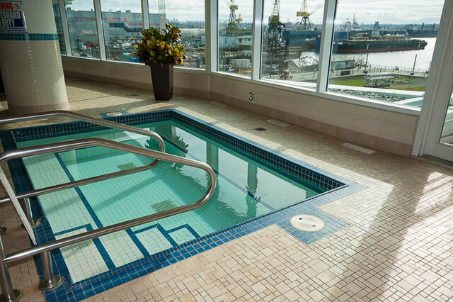 Spacious living room with a serene indoor pool and a stunning cityscape view. - 912 - 175 Victory Ship Way, North Vancouver