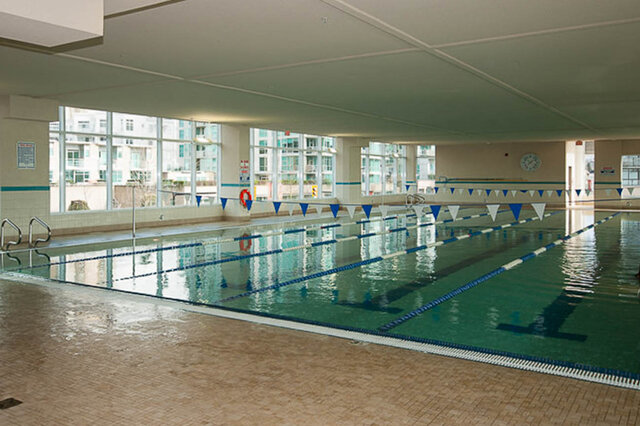 Spacious indoor swimming pool with clear water, lane dividers, and city view through large windows. - 912 - 175 Victory Ship Way, North Vancouver