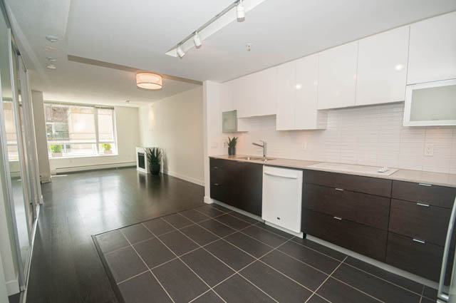 Bright kitchen with dark wood cabinets and granite countertops, featuring a city view through the window. - 103 - 175 West 2nd, North Vancouver
