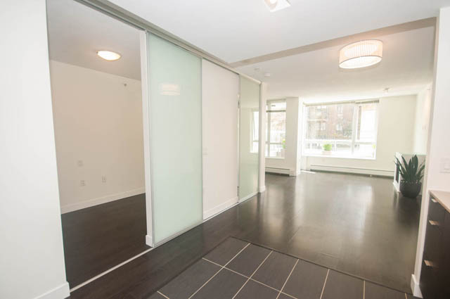Bright kitchen with granite countertops and hardwood floors, leading to a cozy living area with a city view. - 103 - 175 West 2nd, North Vancouver