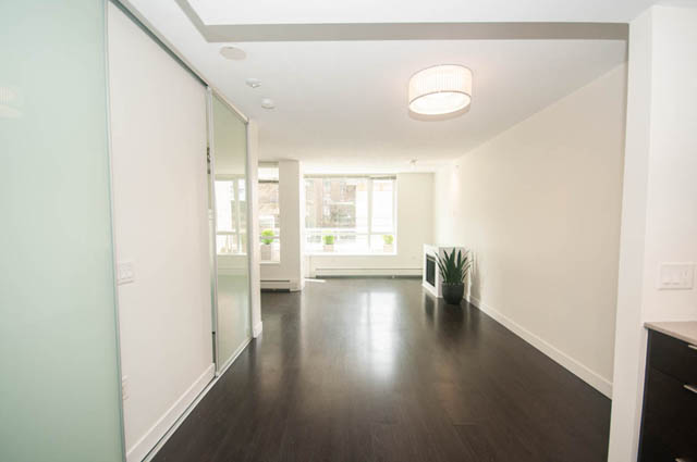 Bright kitchen with modern white cabinets and hardwood floors, leading to a spacious living area with a city view.
