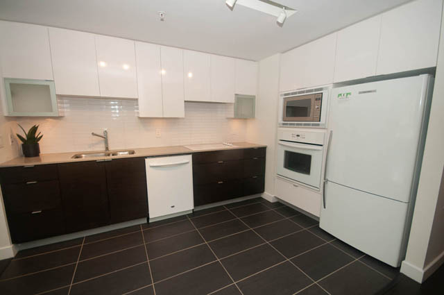 Bright kitchen with white cabinets, black countertops, and dark tiled floors. - 103 - 175 West 2nd, North Vancouver