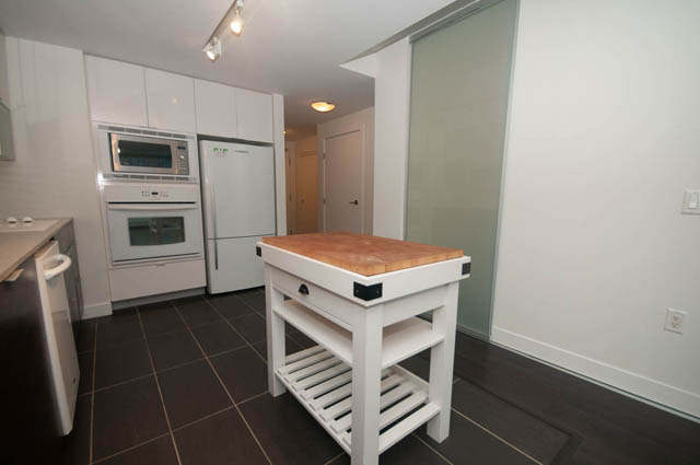 Bright kitchen with white cabinetry and a modern island, featuring a sleek countertop and dark flooring. - 103 - 175 West 2nd, North Vancouver