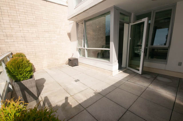 Bright patio with sliding glass doors, brick wall, and potted plants. - 103 - 175 West 2nd, North Vancouver